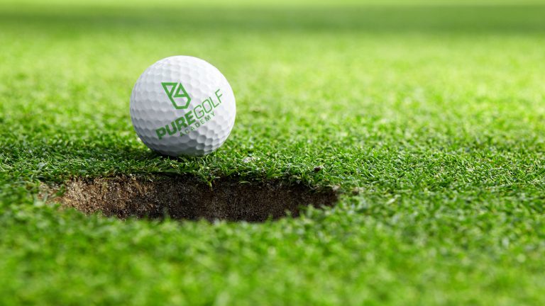 A photograph of a gold ball on a gold green. The ball is printed with the Pure Golf logo, designed by Born + Raised.
