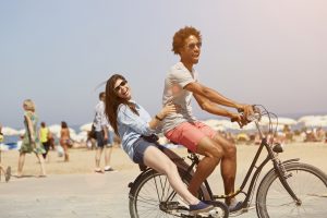 Side view of multi-ethnic couple riding bicycle at beach