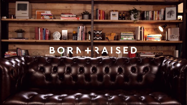 Born and Raised logo over background of sofa and shelves